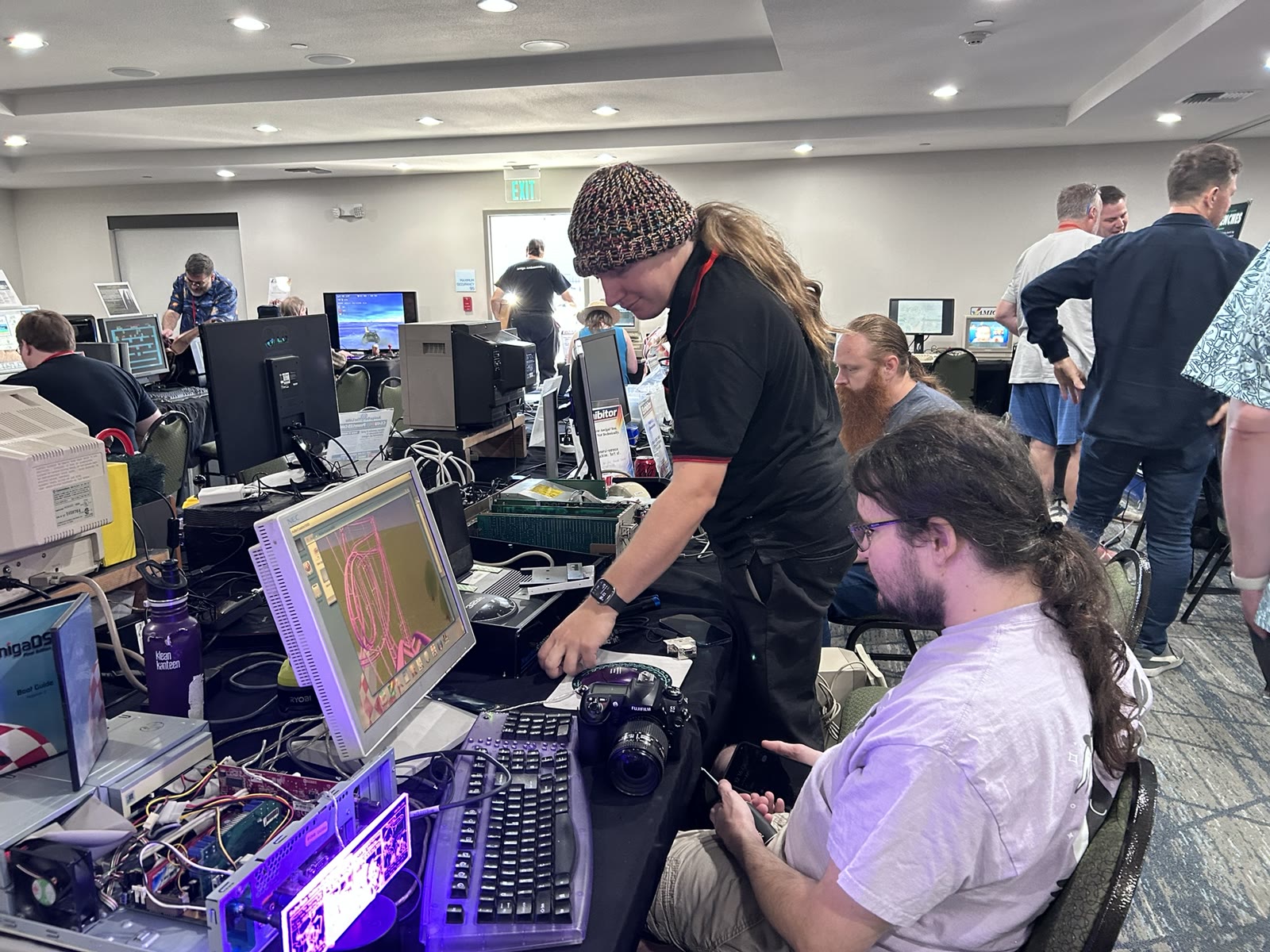 Hands-on AmiWest hardware with an open computer and a display surrounded by attendees